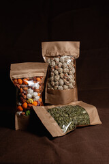 Assortment of glazed nuts and pumpkin seeds in paper bags as healthy snack on brown background in dark studio 