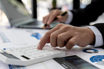 Businessman using a calculator to calculate numbers on a company's financial documents, he is analyzing historical financial data to plan how to grow the company. Financial concept.