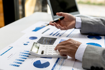 Businessman using a calculator to calculate numbers on a company's financial documents, he is analyzing historical financial data to plan how to grow the company. Financial concept.