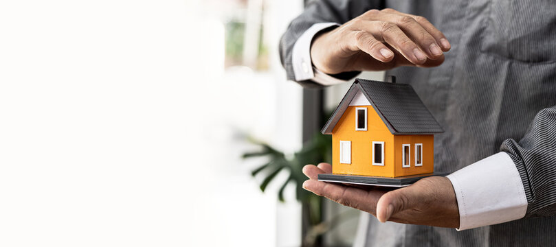 Person puts her hand on top of a miniature house model, photo of home insurance concept, when buying a new home should have home insurance to be sure if there is any danger to the home.