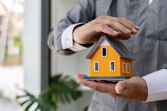 Person puts her hand on top of a miniature house model, photo of home insurance concept, when buying a new home should have home insurance to be sure if there is any danger to the home.