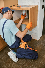 Bearded male plumber repairing pipe in kitchen