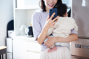 赤ちゃんを抱きながらスマートフォンを操作する女性