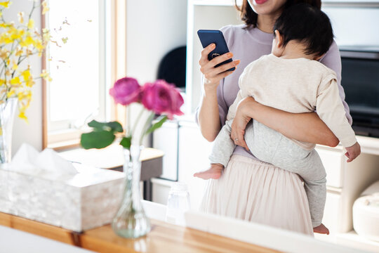 赤ちゃんを抱きながらスマートフォンを操作する女性