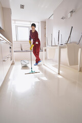 Focused experienced Caucasian cleaning lady mopping kitchen
