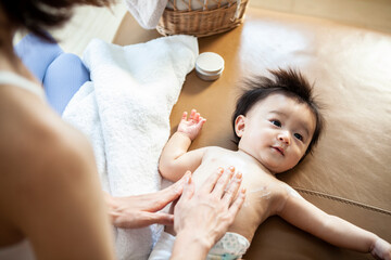 赤ちゃんの肌に保湿クリームを塗る母親