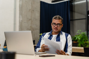 Man reading documents near laptop
