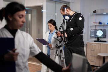 Researcher doctor looking at monitor analyzing heart rate pulse while sportman running on gym trainer working at body endurance during medical workout in modern lab. Physician monitoring EKG data