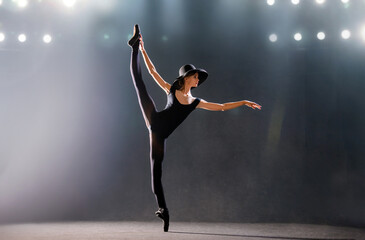 ballerina in tight-fitting suit is dancing on black background on pointe shoes, silhouette is illuminated by sources of color.