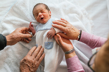 Newborn baby and grandparents' hands caressing him.