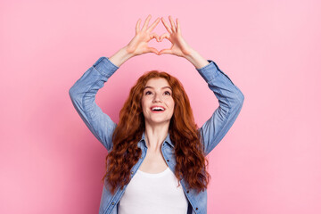 Photo of charming dreamy woman wear denim shirt showing fingers heart looking empty space smiling isolated pink color background