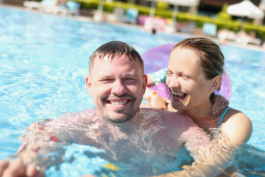 Cheerful couple posing for picture in swimming pool in luxury resort