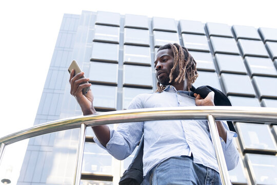 Black young man with dreadlocks checking message in cellphone