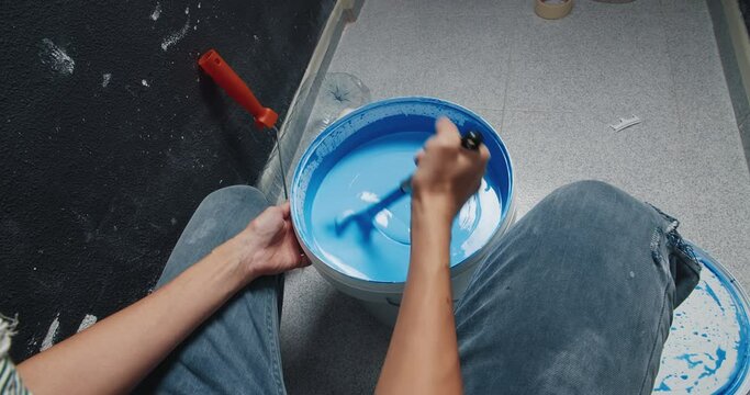 Point of view POV young painter woman mixing blue paint in the bucket preparing for home improvement and repainting the walls. Concept of diy home repairs 