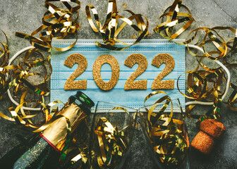 New Years Eve celebration concept background. Medical mask with the numbers 2022 and Champagne bottle with glasses .Covid-19 New Year concept