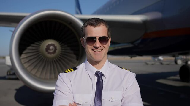 Airport, pilot, airplane. Portrait of confident male pilot in uniform smilingin background turbine of plane, aircraft, Travel professional captain travelling transportation professions people concept