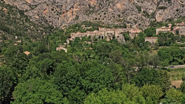 Moustiers Sainte Marie France Aerial v1 establishing shot low level drone flyover historic ancient village capturing beautiful townscape with medieval architecture toward rocky ravine - July 2021