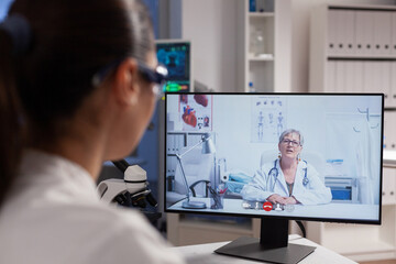 Therapist doctor discussing vaccine development with remote chemist woman during online videocall meeting conference in hospital laboratory. Medicine teleconference call on computer screen