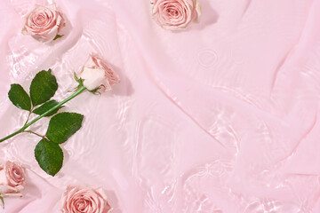 Flowers composition. Pink silk fabric background with flowers and bouquet in water, flat lay, copy space. Valentines or woman's day minimal concept. Nature bloom idea.