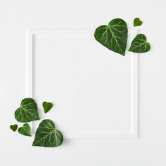 Creative layout made with heart shape leaves and white frame, flat lay, top view. Valentines or woman's day minimal concept. Nature background.