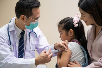 Young Asian girl get medical vaccine injection from the doctor with her mother sit and hold to support. Medical service for young people, kids.