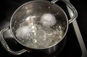 Two white eggs are boiled in a saucepan.