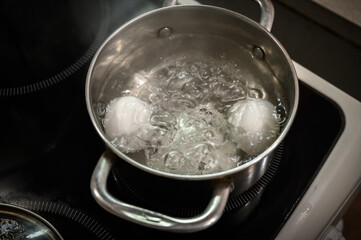 Two white eggs are boiled in a saucepan.