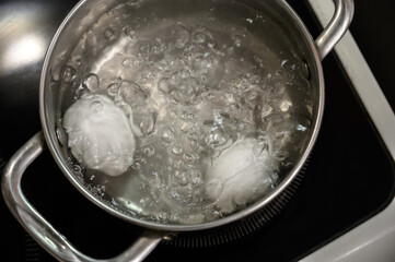 Two white eggs are boiled in a saucepan.