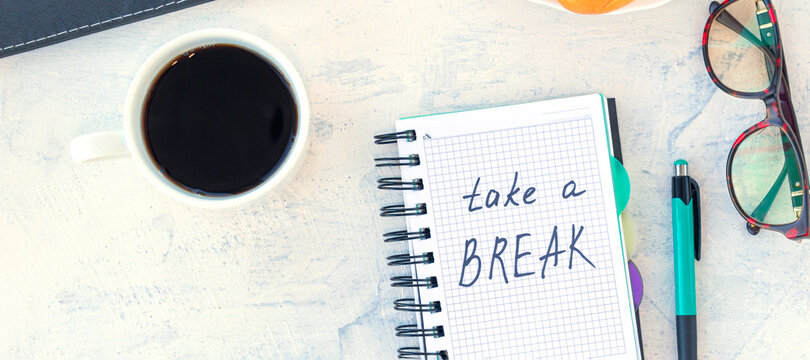 banner with Take a break. Concept time off. Words Take a break in a notebook on the working table with cup of coffee and bun.