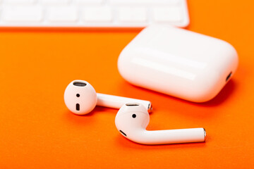 White wireless earphones with charging case on bright orange background