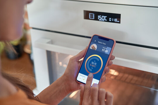Woman adjusting oven temperature on smart phone at modern home