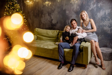 Obraz premium Young beautiful family with two daughters in smart clothes are hugging in the living room, celebrating the christmas holiday