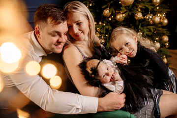 Obraz na płótnie Canvas Young beautiful family with two daughters in smart clothes are hugging in the living room, celebrating the christmas holiday