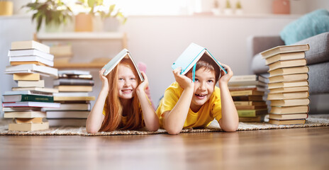 Two cute children lying on the floor indoors with books on the head