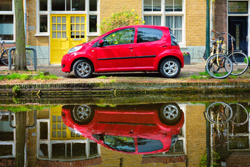 Red car on canal embankment in street of Delft. Delft, Netherlands