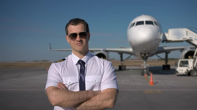 Airport, pilot, airplane. Portrait of confident pilot in uniform keeping arms crossed on runway in background commercial plane, aircraft, Travel professional travelling flight safety, aviation people
