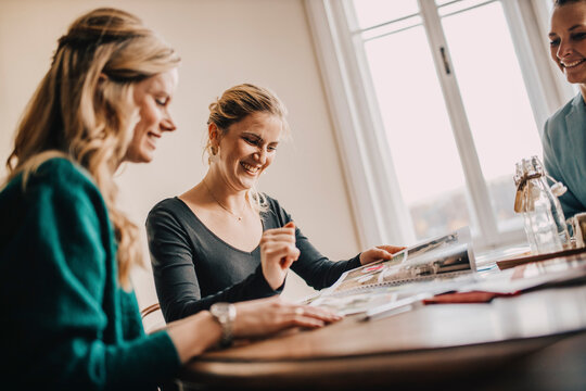 Smiling female event planners looking at photo album while sitting together