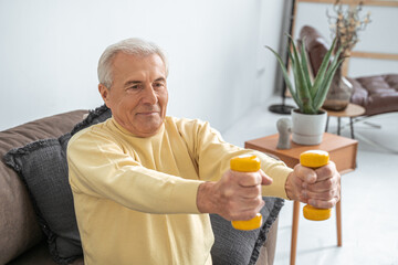 Senior man exercising at home while sitting on the couch