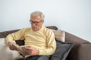 Thoughtful aged man reading favorite literature at cozy home