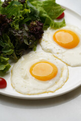 Two fried eggs and fresh salad leaves in white plate