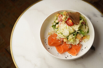 Caesar salad with salmon fish on white bowl