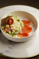 Caesar salad with salmon fish on white bowl