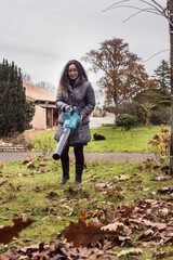 Mature woman picking up leaves in the garden with her electric blower