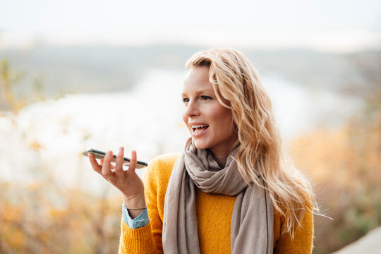 Blond woman sending voicemail through smart phone during autumn