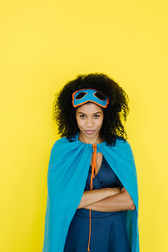 Afro woman wearing superhero costume standing against yellow background
