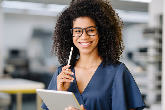 Smiling female entrepreneur holding digital tablet and digitized pen standing in office