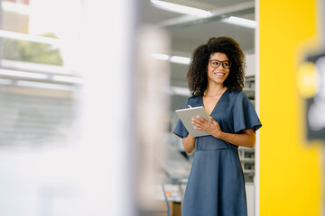 Smiling businesswoman looking away while holding digital tablet at office