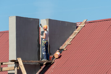 A construction team is installing a new ventilation pipe or fireplace on the roof of the building. New concrete pipe on the roof made of red tiles. Repair of the roof and facade.