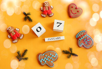 Calendar for January 7: cubes with numbers 0 and 7, the name of the month in English among gingerbread in the form of men, hearts, mittens and fir branches, yellow background, top view, bokeh