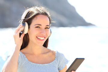 Happy woman listening to music looking at camera on the beach